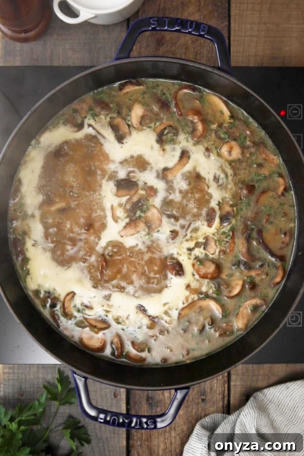 Homemade cream of mushroom soup gently simmering in a black enameled cast iron Dutch oven, filling the kitchen with its aroma.