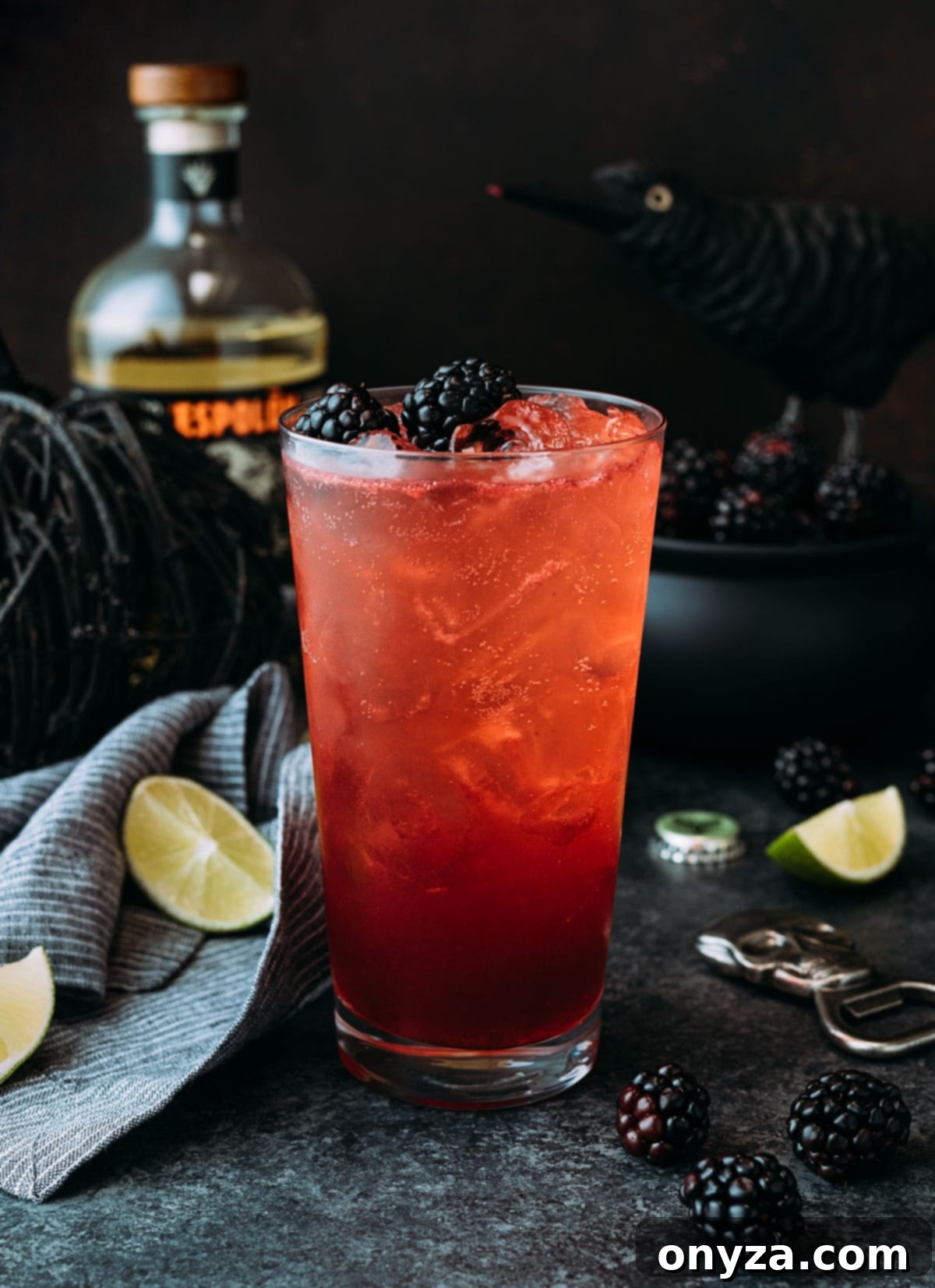 A stunning Blackberry El Diablo cocktail, garnished with frosted blackberries and a lime wheel, prominently featured in a charming Halloween-themed vignette. Decorative elements like a small pumpkin, autumn leaves, and subtle spooky accents create a festive and inviting atmosphere around the drink, emphasizing its seasonal appeal.