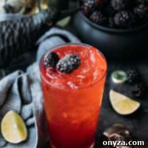 The Blackberry El Diablo cocktail in a highball glass, elegantly presented within a Halloween setting, showcasing its vibrant red color and fresh berry garnish. This visual highlights its appeal as a festive adult beverage perfect for spooky celebrations.