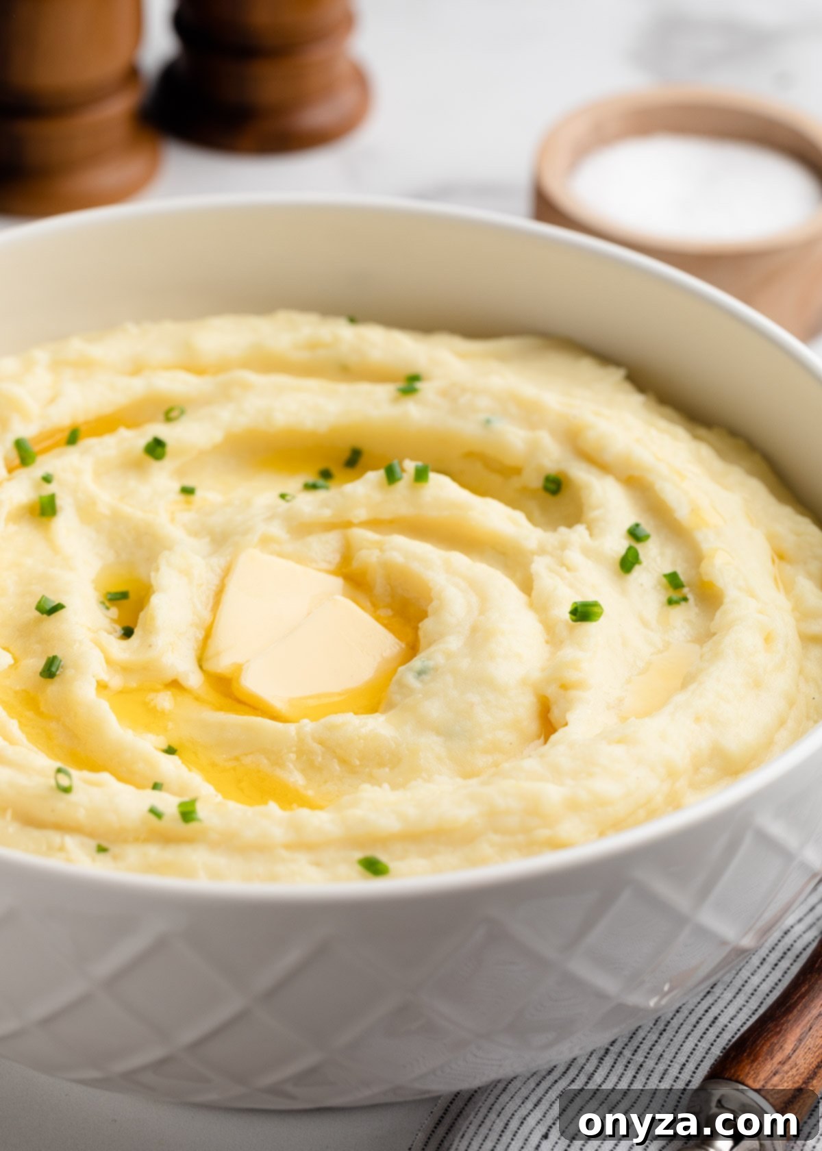 Cream Cheese Mashed Potatoes in a white serving bowl with pats of butter and snipped chives