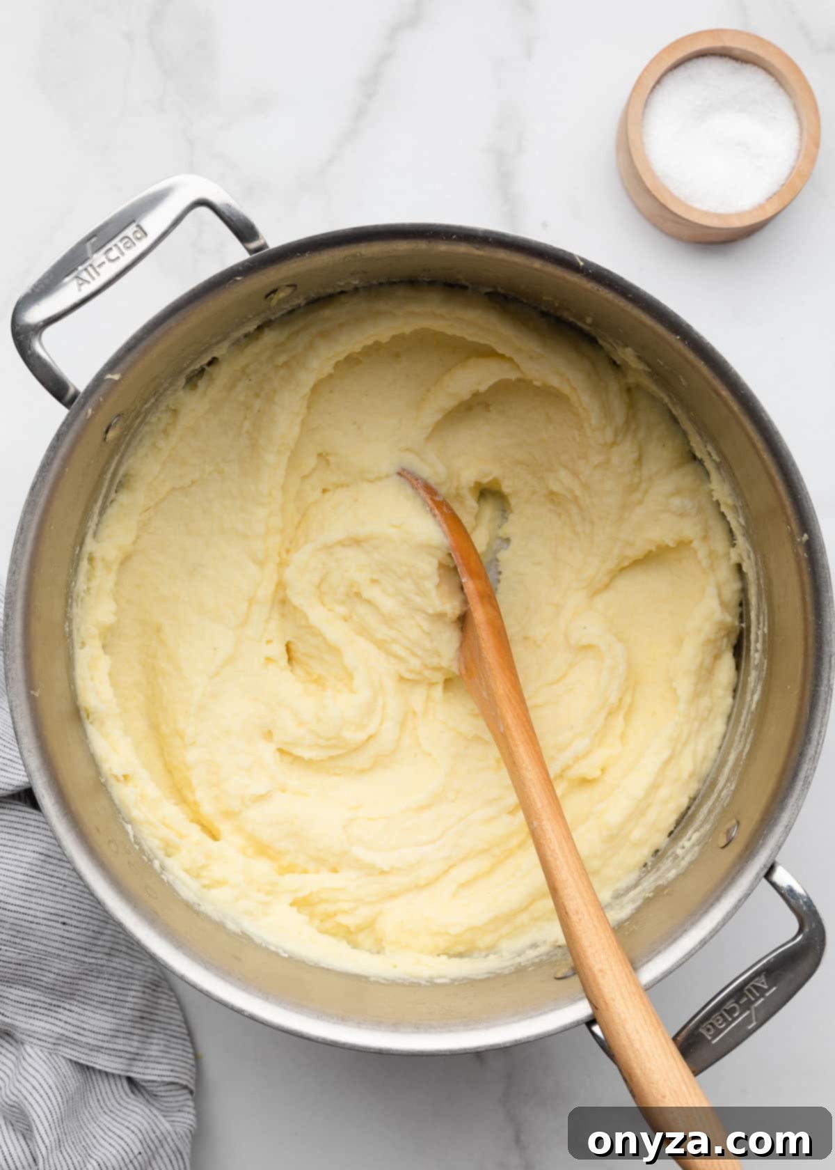 Overhead of cream cheese mashed potatoes in a stainless steel pot with a wooden spoon