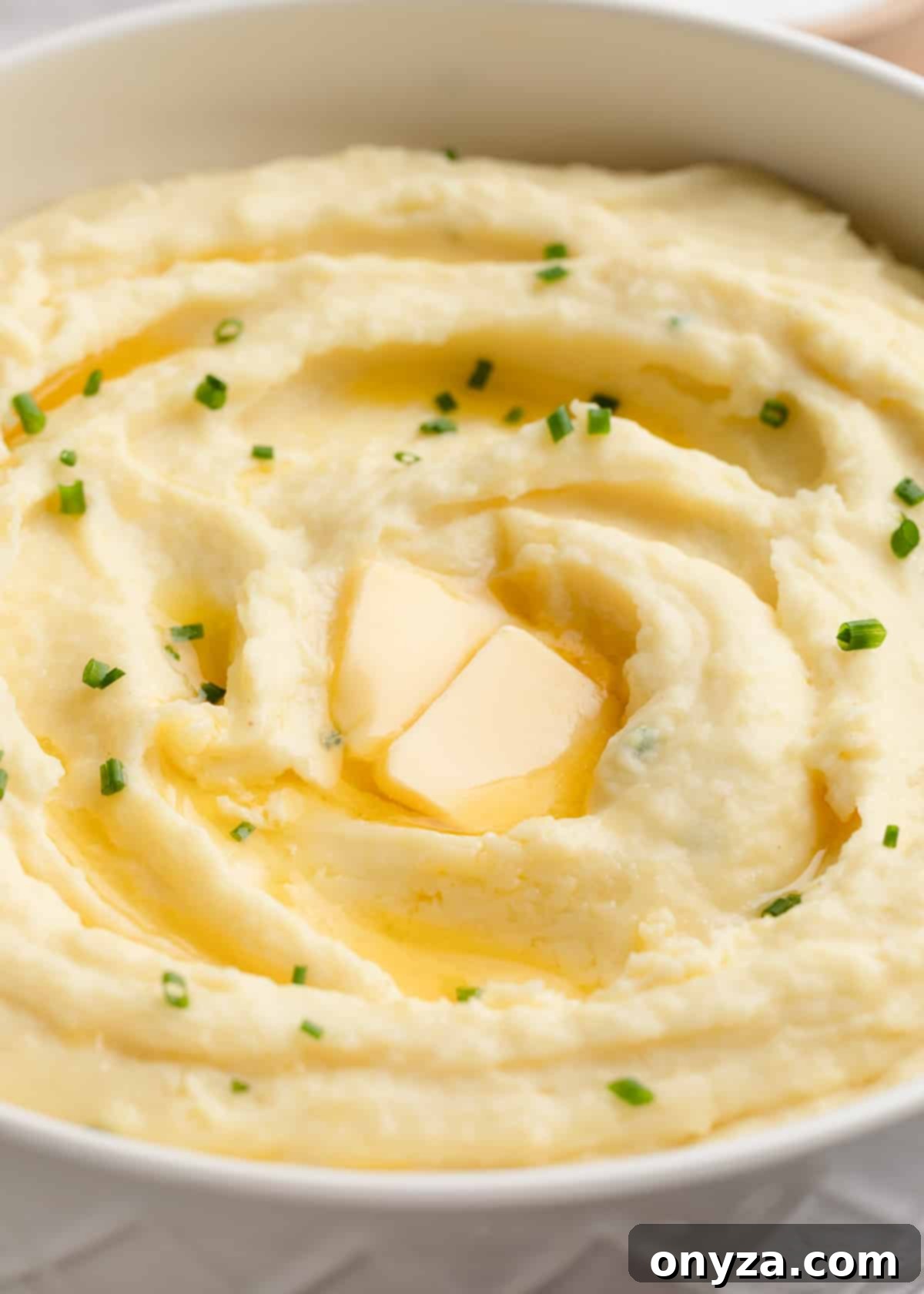 Closeup of cream cheese mashed potatoes garnished with pats of butter and chives in a white bowl