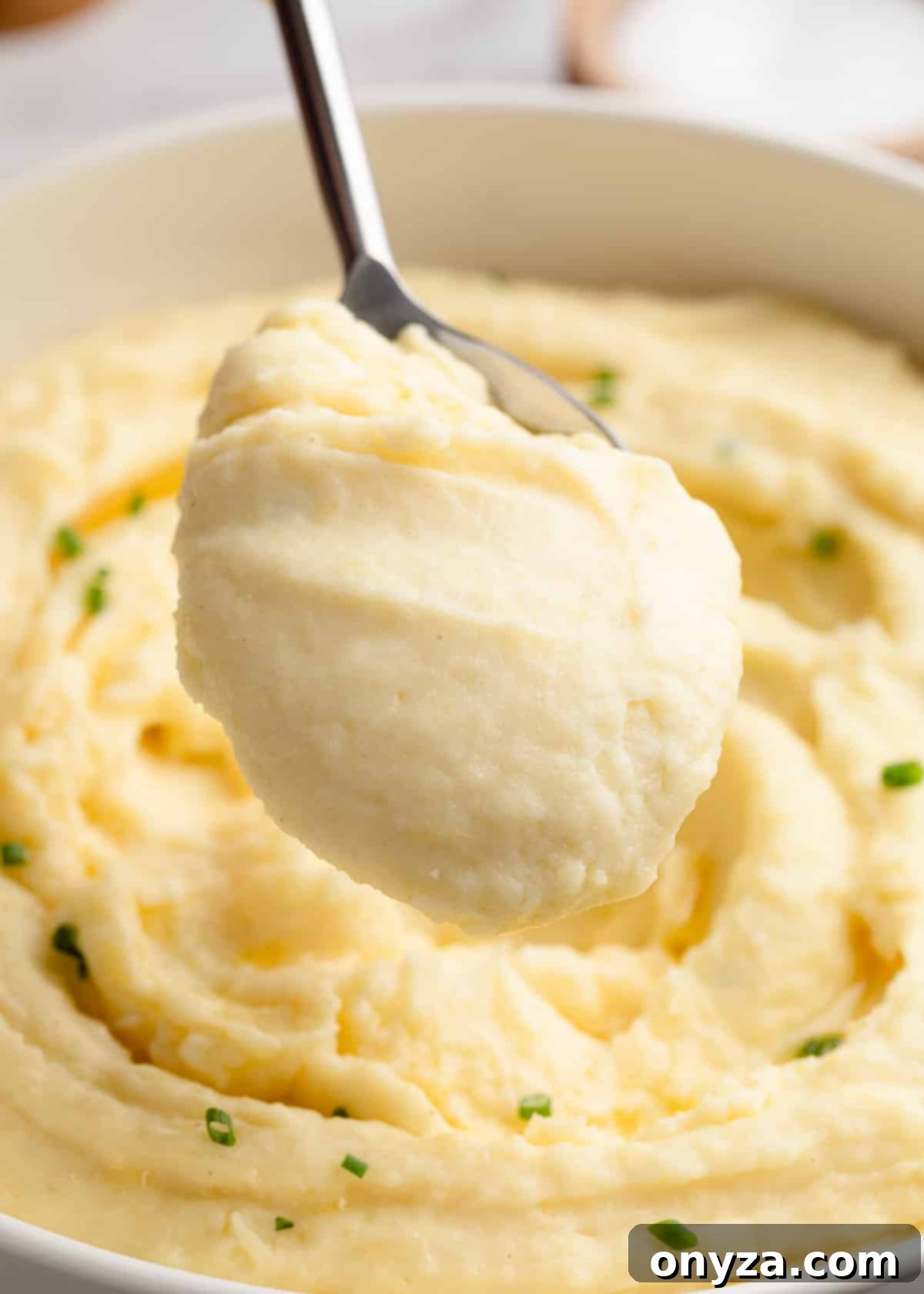 A scoop of cream cheese mashed potatoes on a serving spoon held over the serving bowl