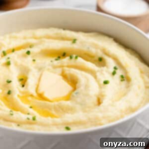Cream Cheese Mashed Potatoes in a white serving bowl with pats of butter and snipped chives