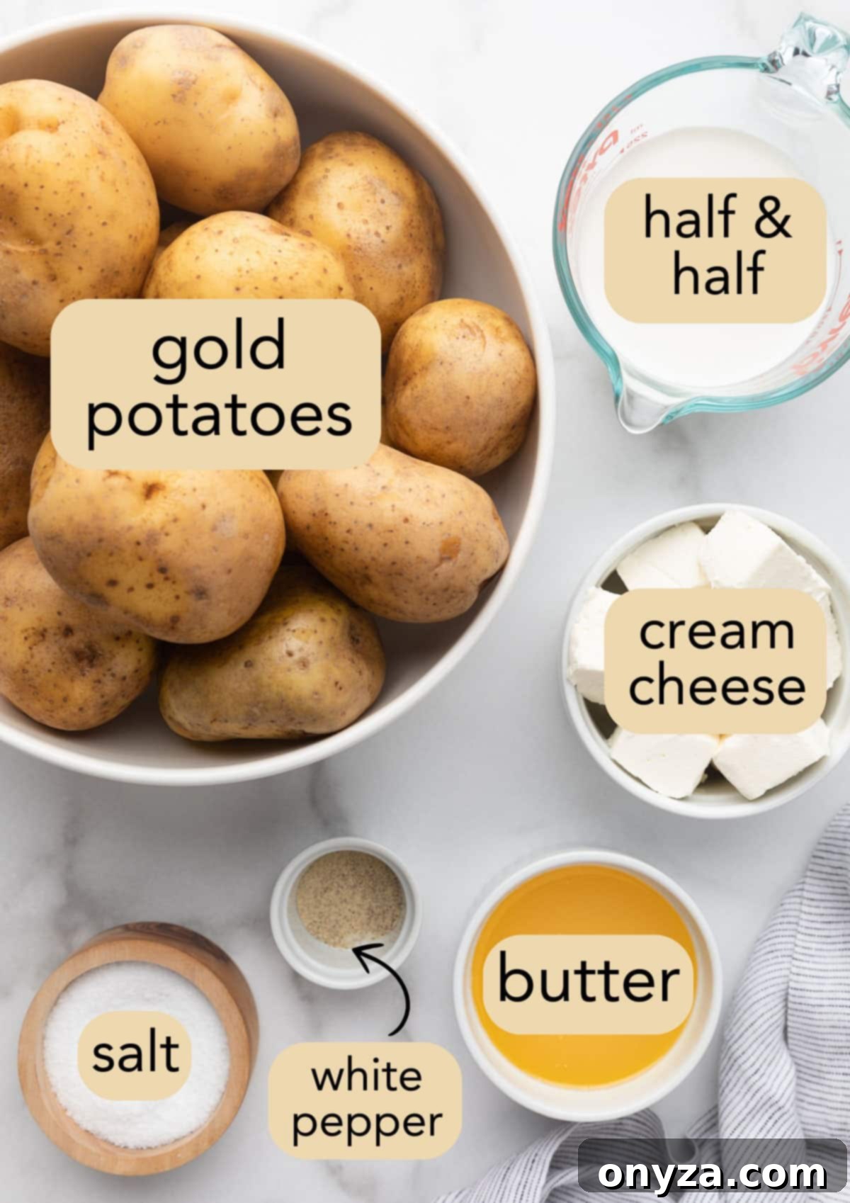 Overhead shot of ingredients needed to make cream cheese mashed potatoes, laid out in bowls on a marble board with text labels.