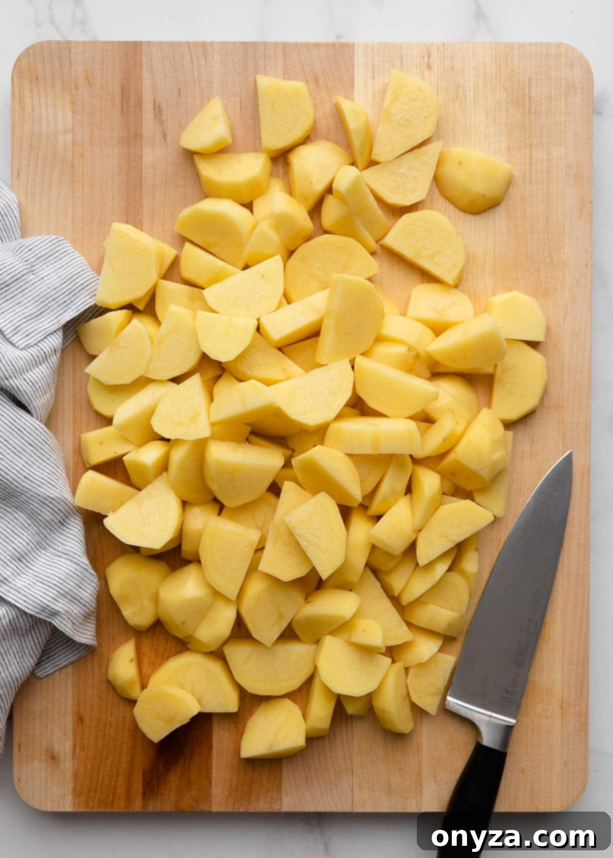 Pile of sliced gold potatoes on a wood cutting board with a chef's knife