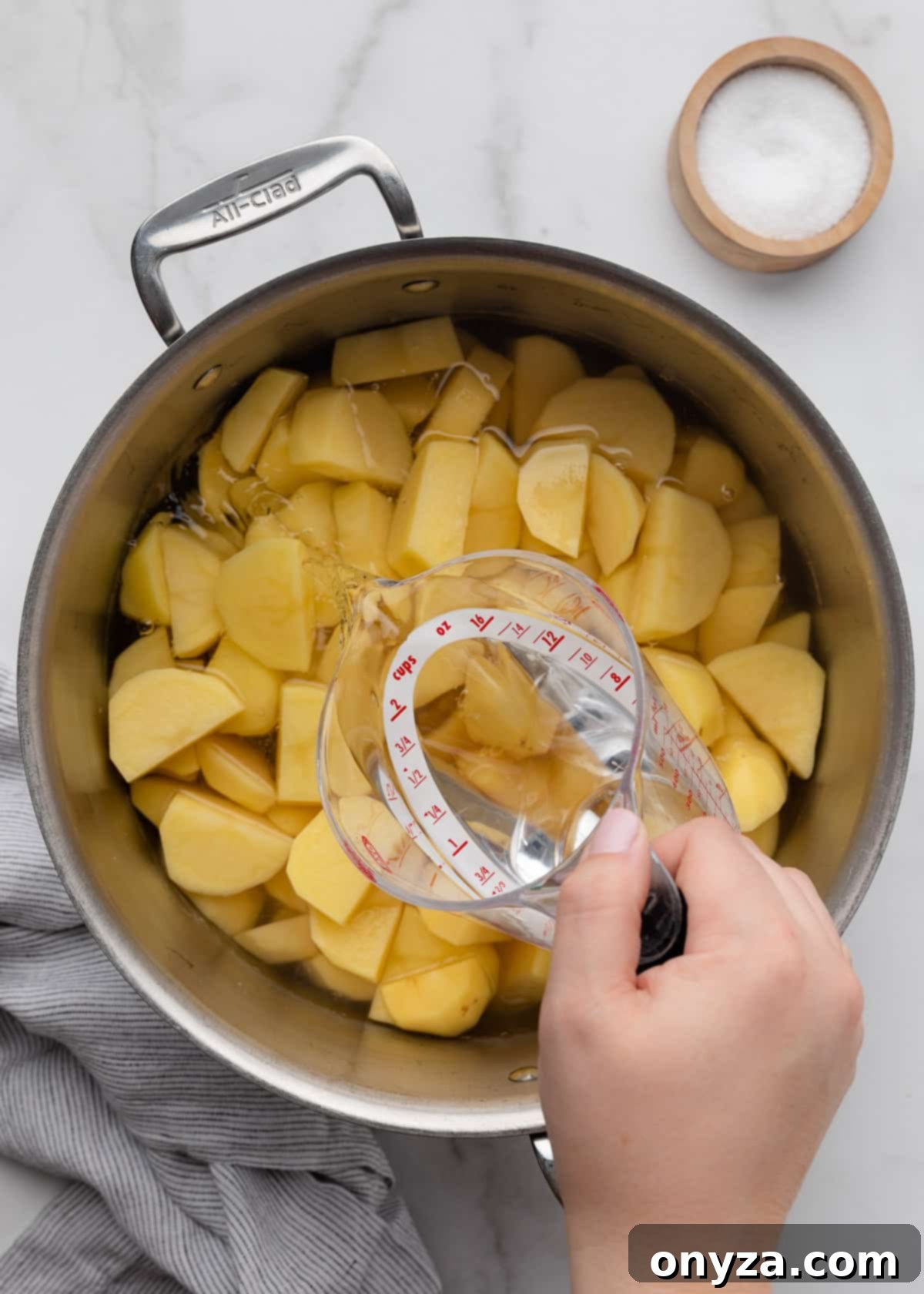 Pouring water into a pot of sliced raw gold potatoes with a liquid measuring cup
