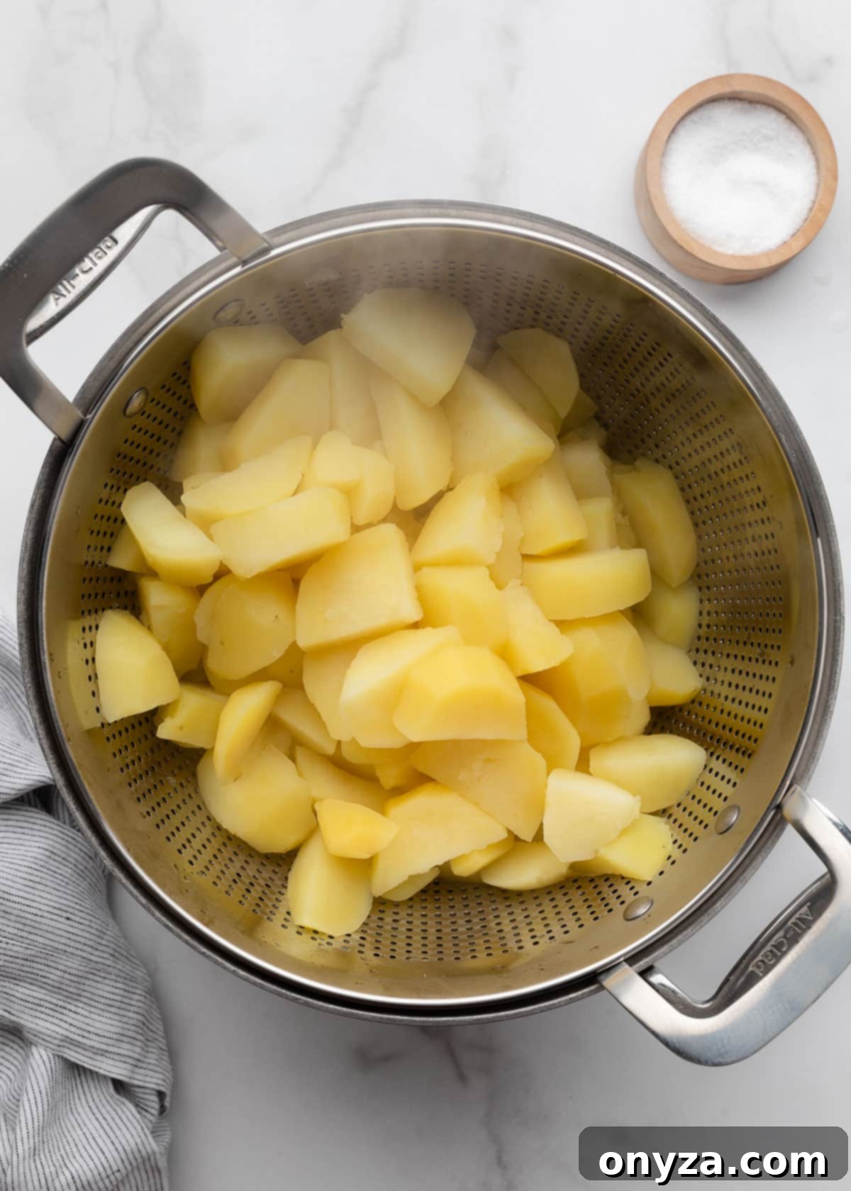 Drained cooked gold potato slices in a stainless steel colander set over a stock pot