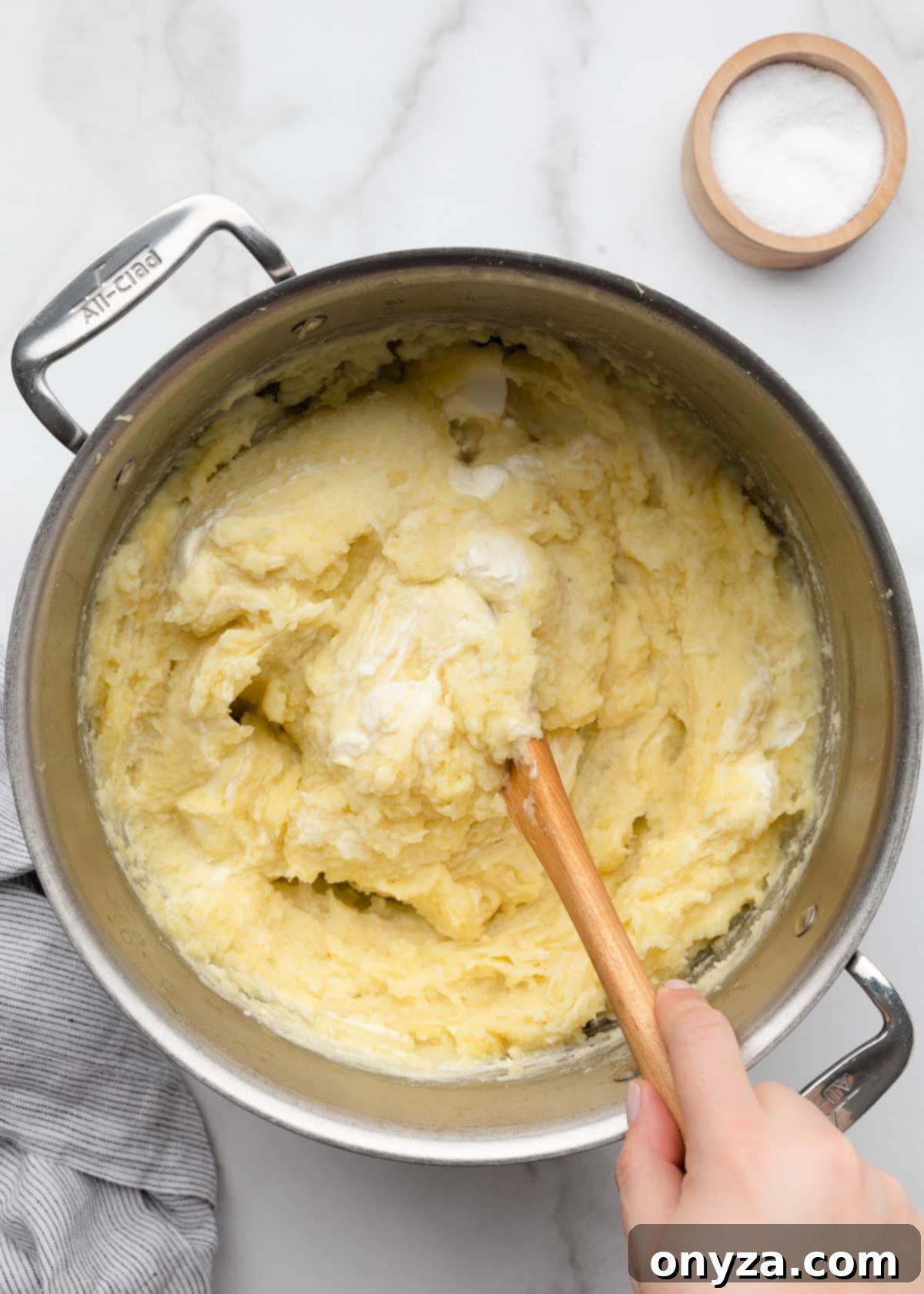 Stirring cream cheese mashed potatoes in a stainless steel pot with a wooden spoon