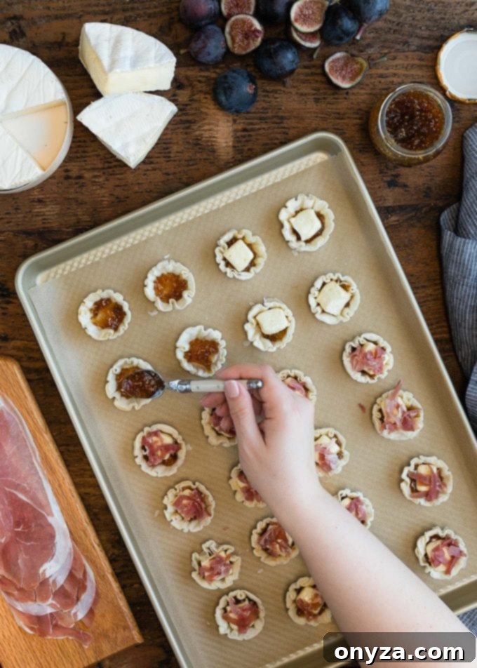 spooning fig jam into miniature phyllo shells on a baking sheet
