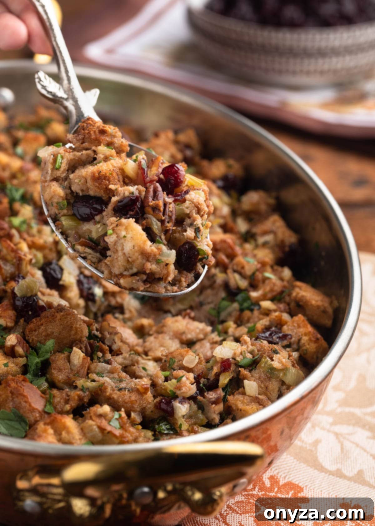 Festive Cranberry Pecan Stuffing 6 silver serving spoon holding a scoop of cranberry pecan stuffing over the baking dish