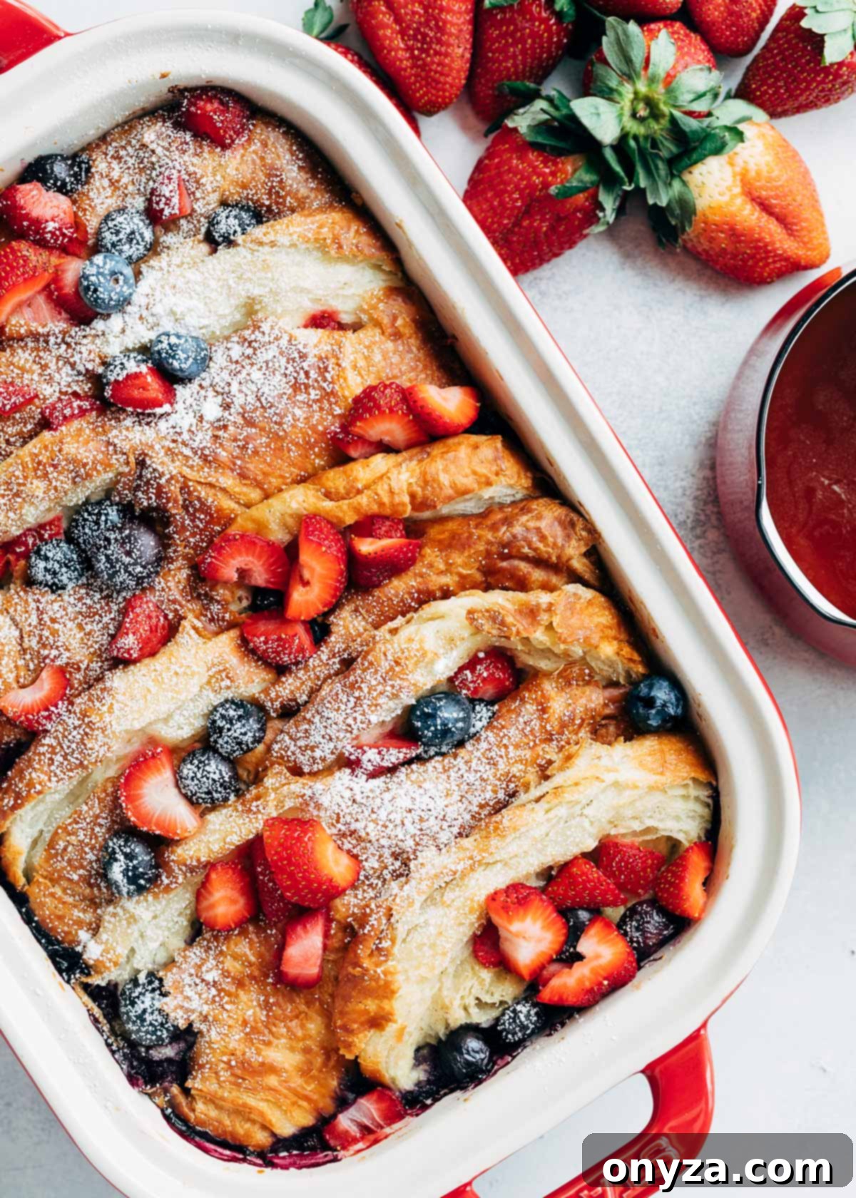 Overhead view of a golden-baked croissant French toast casserole generously topped with fresh berries, served in a rustic rectangular baking dish, ready to be enjoyed.