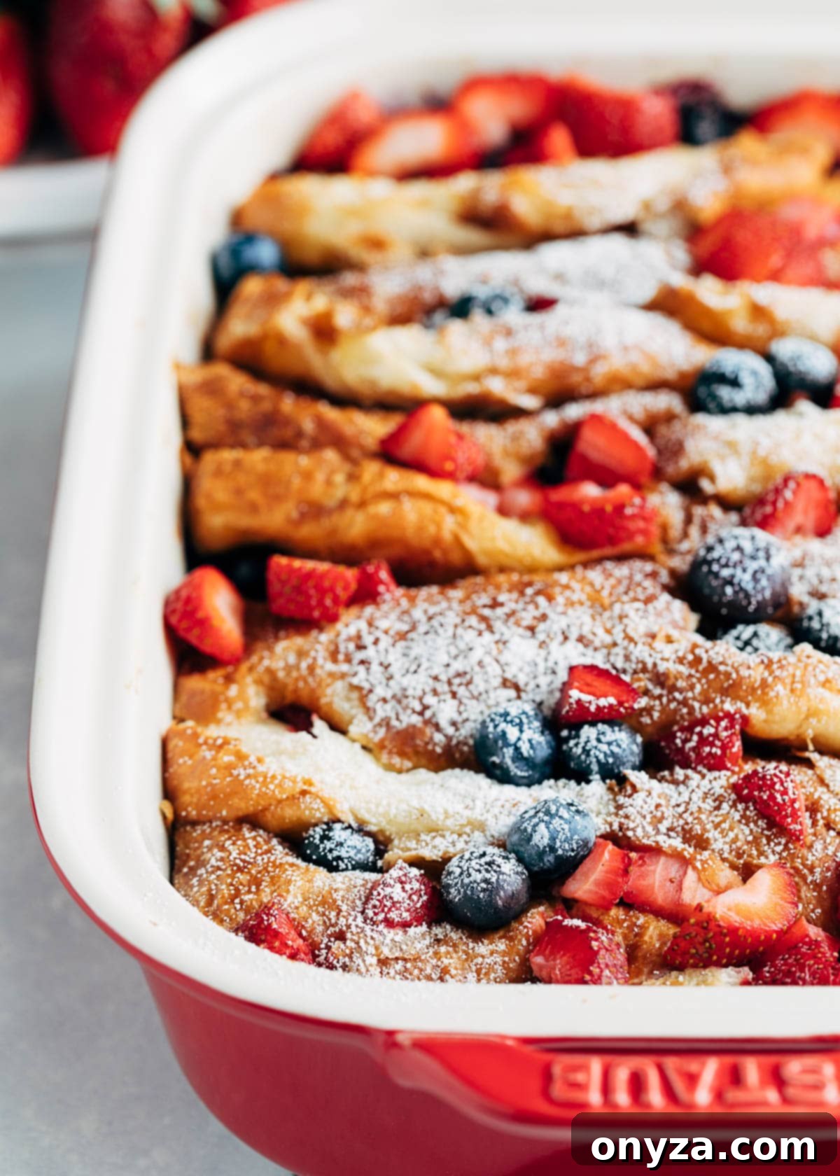 Side view of a perfectly baked, golden-brown croissant French toast casserole, lightly dusted with powdered sugar and still warm and inviting in its rectangular baking dish, ready for serving.