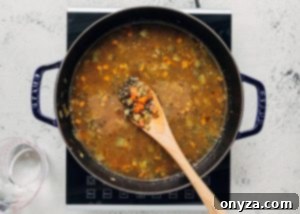 A pot of lentil soup simmering with broth, water, and herbs, creating a rich aroma.