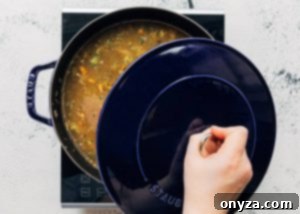 A lid being placed partially on a Staub cast iron pot, allowing the soup to simmer gently.