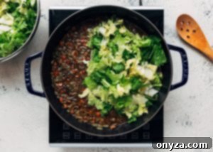 Chopped raw escarole being added to a pot of lentil soup, ready to wilt down.