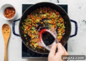 Deglazing a pot of sautéed vegetables with red wine, scraping up the flavorful browned bits.