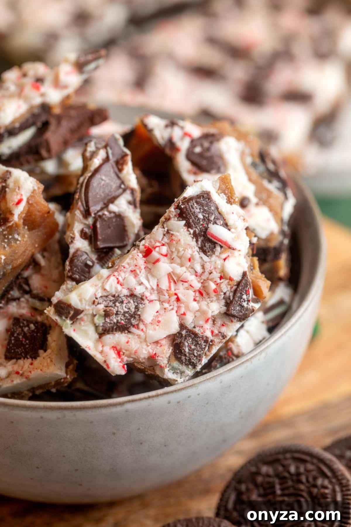 Close-up of Oreo chocolate mint toffee bark in a gray bowl, topped with crushed peppermint candies and chunks of Oreo cookies.