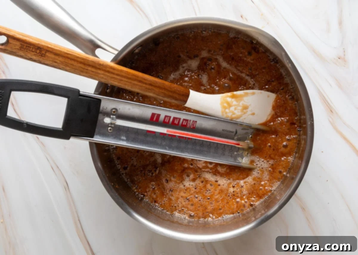 Dark golden toffee bubbling in a saucepan on the stove, with a candy thermometer attached.
