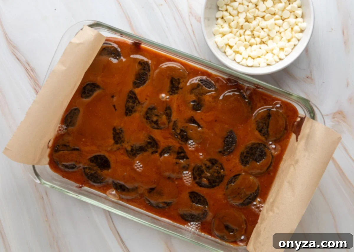 Hot toffee being poured over a layer of Oreo cookies on top of melted chocolate in a baking dish.