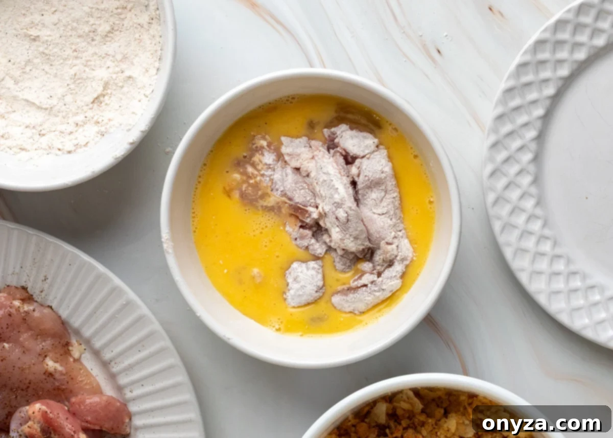 Dipping chicken into the egg wash.