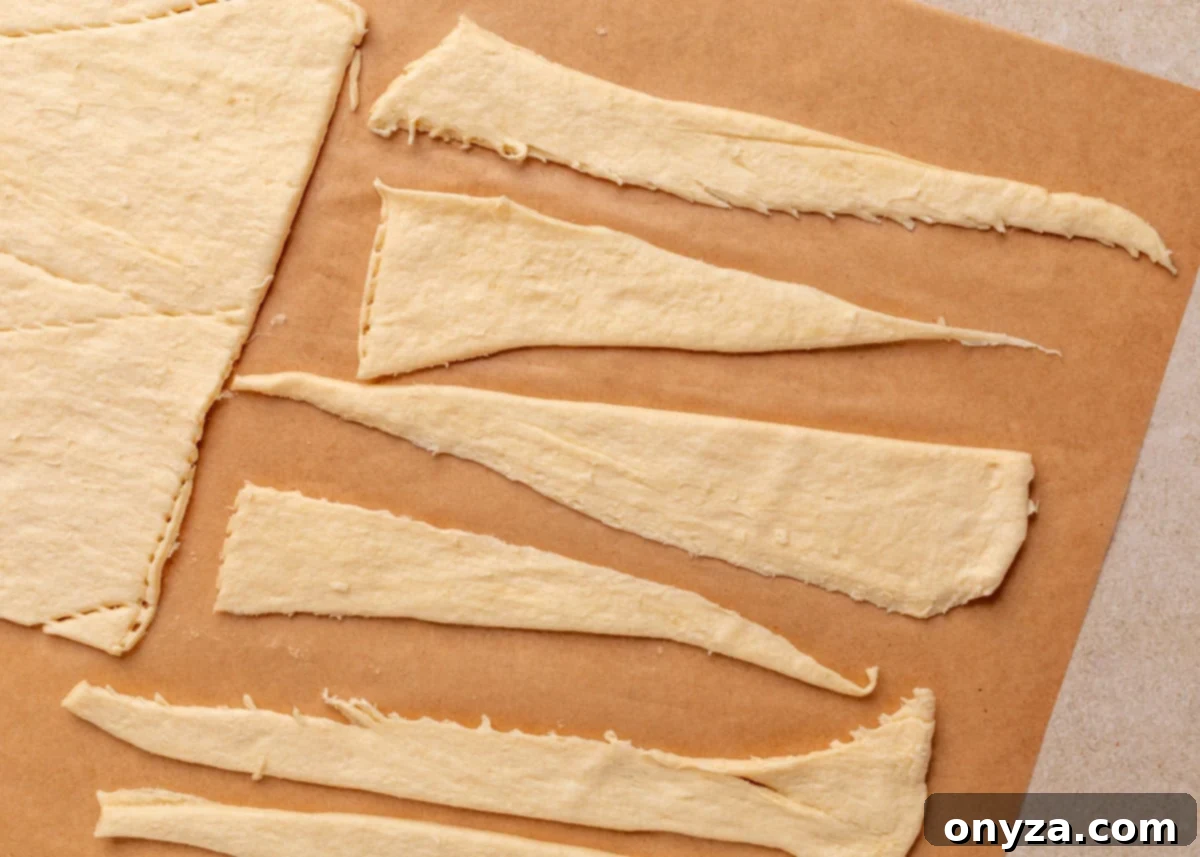 Unrolled crescent dough triangles arranged on a sheet of parchment paper, ready to be filled and rolled for Jalapeño Popper Pigs in a Blanket.
