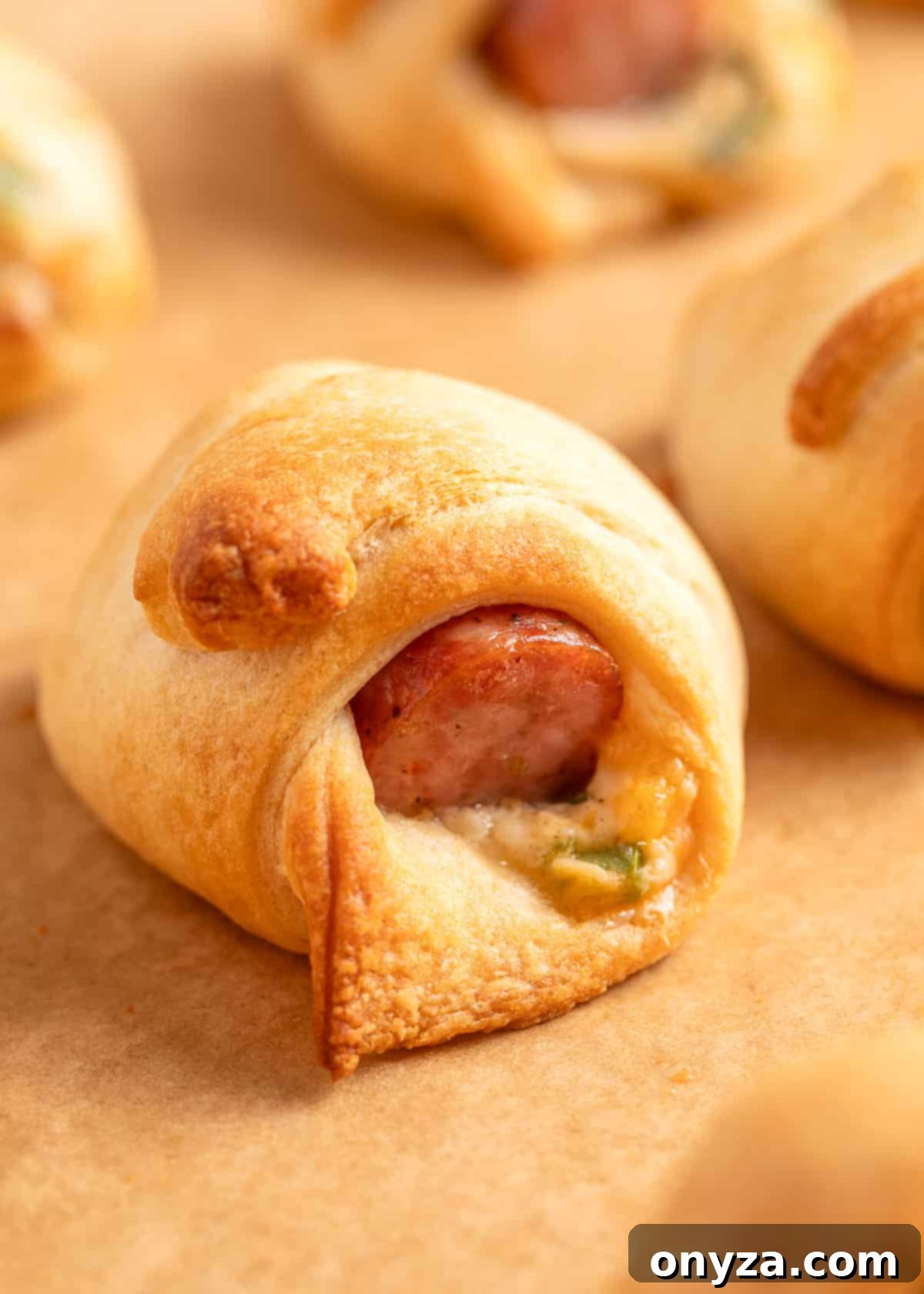 Close-up of a baked jalapeño popper pig in a blanket on parchment paper, showing golden-brown crescent dough wrapped around smoked sausage and oozing jalapeño cream cheese filling.